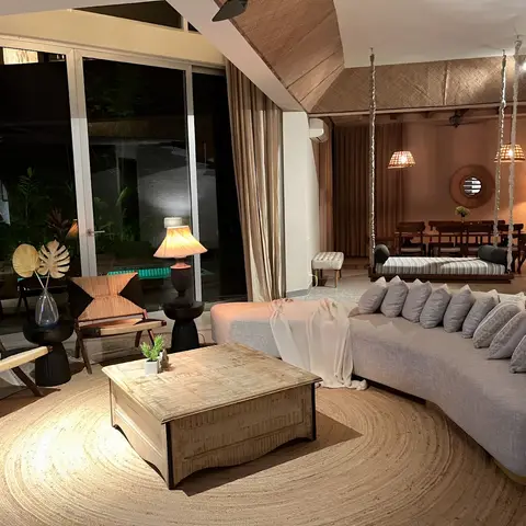 An open lounge with a curved grey sofa and woven rope armchairs around a wooden trunk coffee table on a round jute rug, a