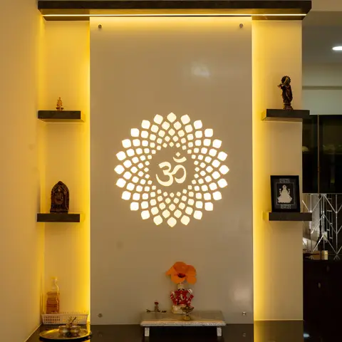 Dedicated pooja unit with a backlit Om-lotus jaali panel, black granite counter, and floating stone shelves for idols.