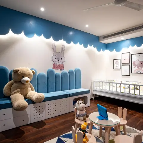 Kids' nursery with a cloud-shaped cove-lit accent wall in blue, a tufted storage bench, a white spindle crib, and a