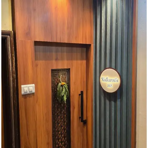 Apartment entrance with a wood-veneer main door featuring a laser-cut metal grille insert, a patterned jaali ceiling panel