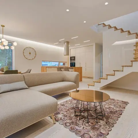 An open living area with a large grey sectional sofa and a mirrored-top wire-base coffee table on a circular patterned rug,