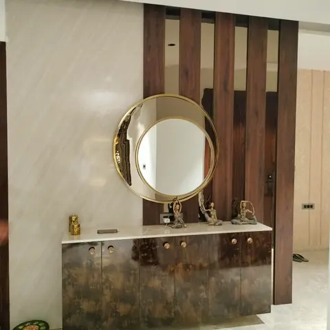 An entrance foyer console area with a round brass-framed mirror above a dark textured-lacquer cabinet with brass knobs, set
