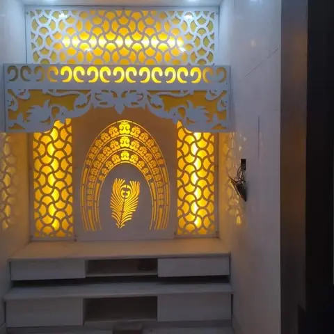 Pooja unit with an ornate white CNC-cut jaali backdrop, a backlit peacock-feather and Om motif, and a marble-look base with