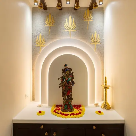 A pooja niche with a backlit arched alcove holding a brass Krishna idol, framed by gold-leaf lotus motifs on a textured