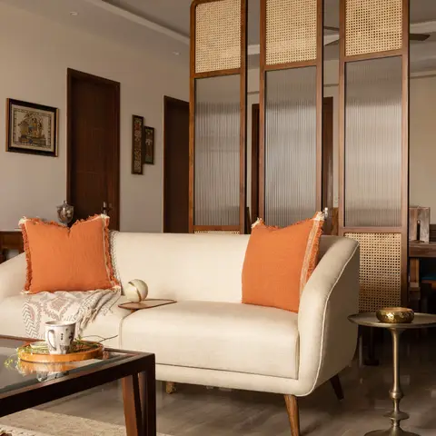 A living room with a cream mid-century sofa and orange linen cushions, in front of a cane-and-reeded-glass room-divider