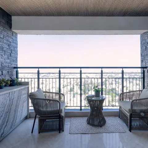 High-rise balcony with stacked-stone side walls, a linear wood-slat ceiling, two woven rattan lounge chairs around a round