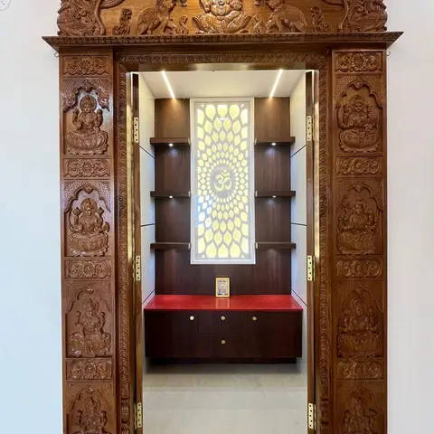 A traditional hand-carved wood pooja unit with Ganesh and Lakshmi relief door panels, a backlit floral Om jaali panel, and a