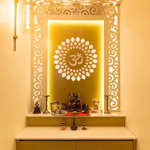 Pooja alcove with an ornate white CNC-cut jaali frame wrapping the wall and ceiling around a backlit Om medallion, brass