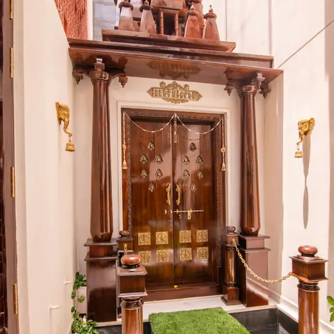 Home entrance with an ornately carved wood double door under a temple-style tiered shikara canopy, flanked by brass elephant