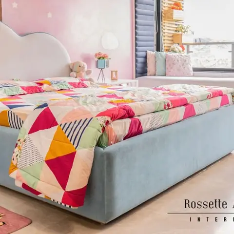 Kids' bedroom with a cloud-shaped upholstered bed in dusty blue, a rainbow patchwork quilt, a pink starred accent wall and a