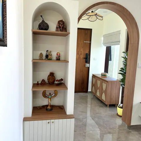 Entryway with an arched display niche of curated curios, a rattan-front console beyond a wood-trimmed archway, and a walnut