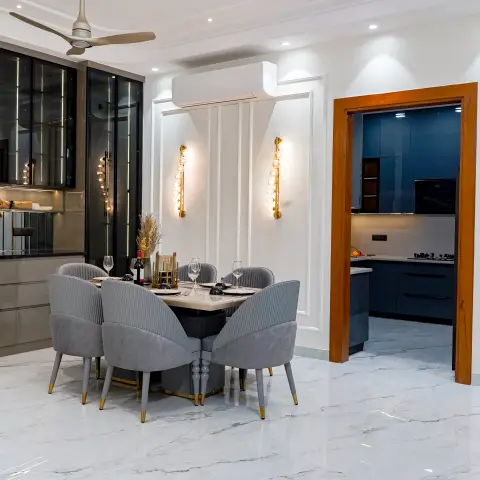 Dining room with a round marble table surrounded by six channel-tufted grey velvet chairs with brass-tipped legs, fluted