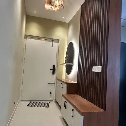 An entrance foyer with a caged pendant light in a wood-clad ceiling recess, fluted wood wall panelling, and a cream storage