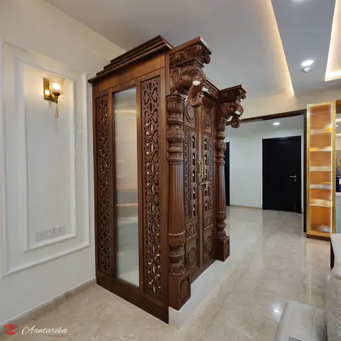 Carved wood pooja unit with elephant-head brackets, jaali screen side panels, fluted pillars, and a gold latch door, set in