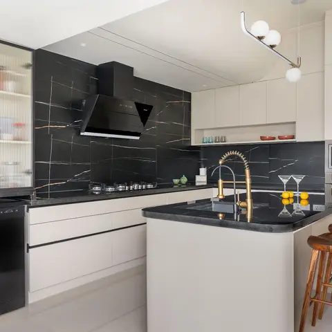 Kitchen with a black marble waterfall-veined backsplash, cream flat-panel cabinetry, a black stone island with a brass