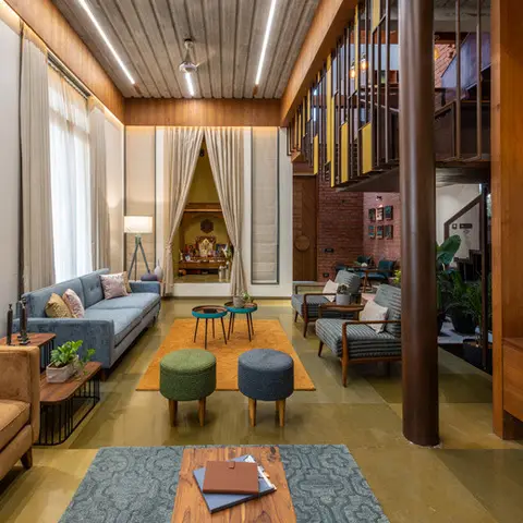 Double-height living room with an exposed wood-slat ceiling and mezzanine above, mismatched blue and mustard sofas, colorful