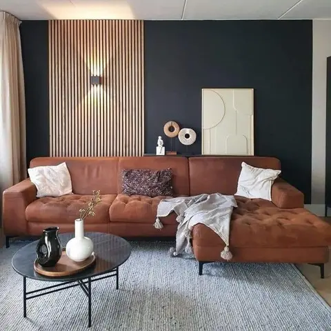 A living room with a cognac leather tufted sectional sofa, a round black coffee table, and a wood-slat accent wall with a