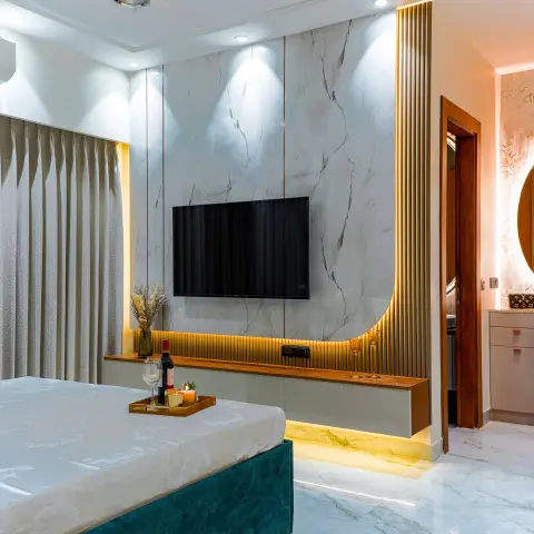 Master bedroom with a book-matched marble TV wall framed by a curved brass-fluted border, a floating walnut console with