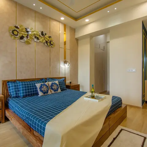 Bedroom with a solid wood bed in blue check linen, a gold metal floral wall sculpture on a brass-inlaid panel wall, and a