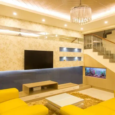 Living room with bright yellow leather sofas facing a mirrored TV wall with floral wallpaper, a built-in aquarium beneath