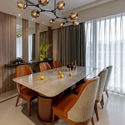 A marble-top dining table on a brass-ringed wood plinth surrounded by eight tan and grey leather chairs, beneath a black