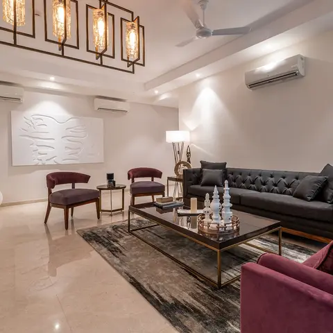 Living room with a charcoal tufted sofa and maroon velvet armchairs around a black-and-brass glass coffee table, beneath a