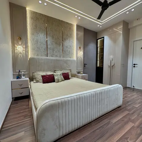 A master bedroom with a channel-tufted cream velvet bed against a gold-trimmed textured wallpaper panel, a cove-lit stepped