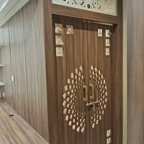 Close view of a pooja room's carved wooden double door with a radiating lotus-petal cutout pattern, brass handles, and a