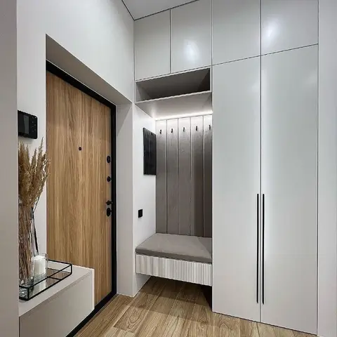 Entrance foyer with a wood-veneer main door, floor-to-ceiling white storage cabinets, and a built-in bench with a fluted