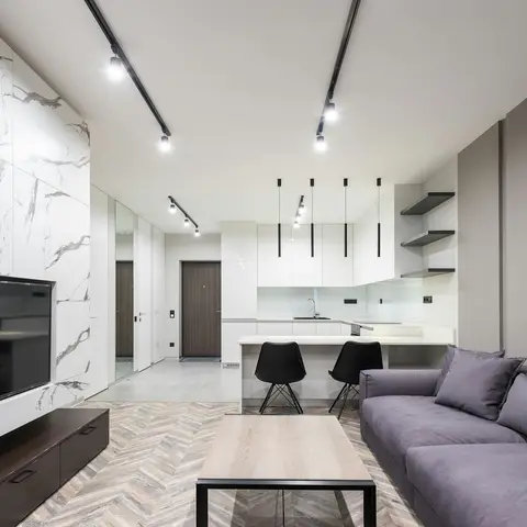 Open-plan living and kitchen with a marble-slab clad TV wall, herringbone wood flooring, a handle-less white gloss kitchen