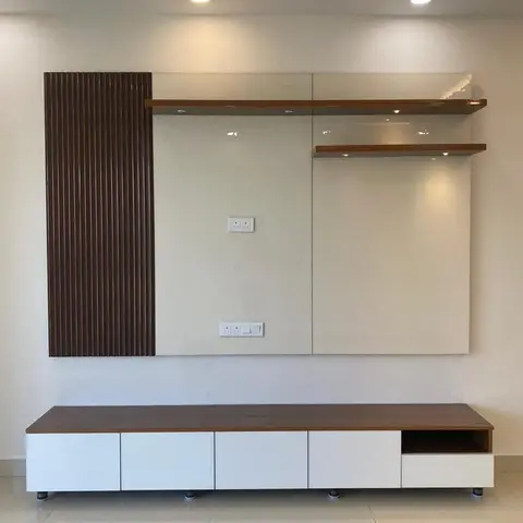 A living room TV wall with a dark walnut fluted panel accent beside a glossy cream backsplash and floating wood shelves,