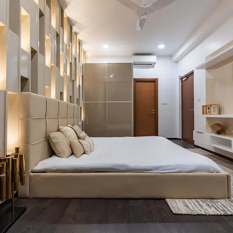 Low beige bed with a tall square-tufted leather headboard, backed by a grid of backlit vertical niches, facing floating