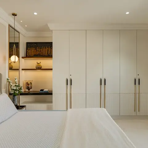 A primary bedroom with a tufted grey leather headboard, a full-height six-door wardrobe with brass pulls and a fluted base,