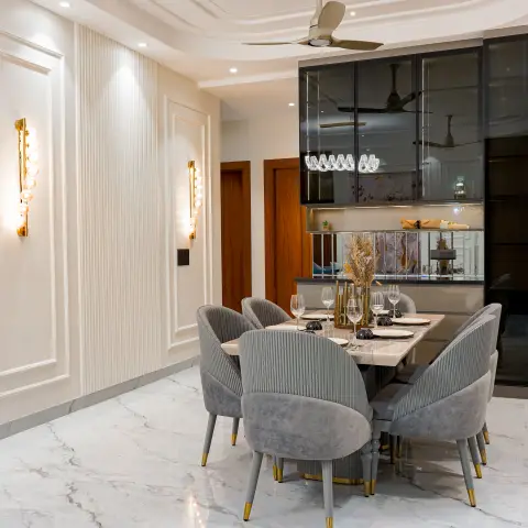 Dining table with six pleated grey velvet chairs under a fluted panel wall, flanked by vertical gold bubble wall sconces and