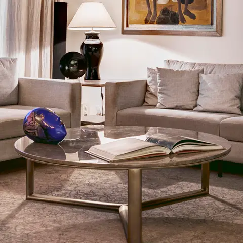 A neutral-toned living room with grey linen sofas around an oval marble-and-brass coffee table styled with a book and a