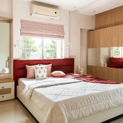 A bedroom with a maroon upholstered headboard, a mirrored wood-finish sliding wardrobe, and a patterned roman blind over the