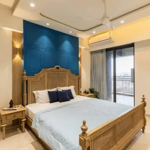 A bedroom with a carved wood cane bed against a deep teal panelled feature wall, cove-lit ceiling, and a glass sliding door