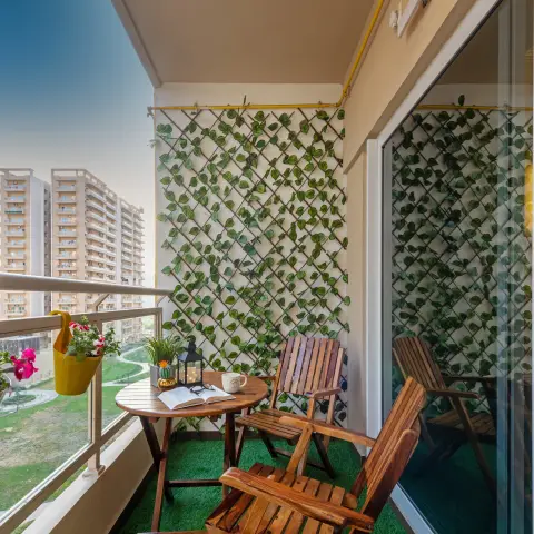 Balcony seating nook with a wooden folding table and chairs on artificial turf, a trellis wall trained with faux ivy, and