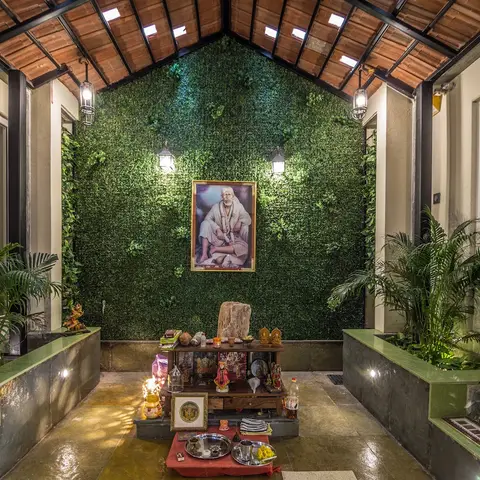 Covered courtyard leading to a pooja altar, framed by a full-height artificial green wall and a pitched clay-tile skylight