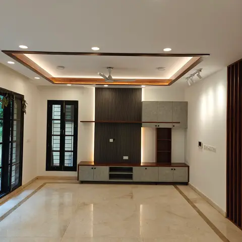 An empty living room with a fluted-panel TV wall flanked by grey cabinetry, a wood-trimmed cove ceiling, and inlay-bordered