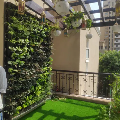 Balcony with a dense vertical garden wall along one side, an artificial turf floor, a wrought-iron railing, and a pergola