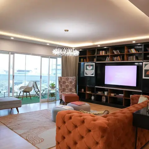 Living room with a tufted rust velvet sofa and patterned wingback chairs facing a full-height black gloss bookshelf-TV wall,
