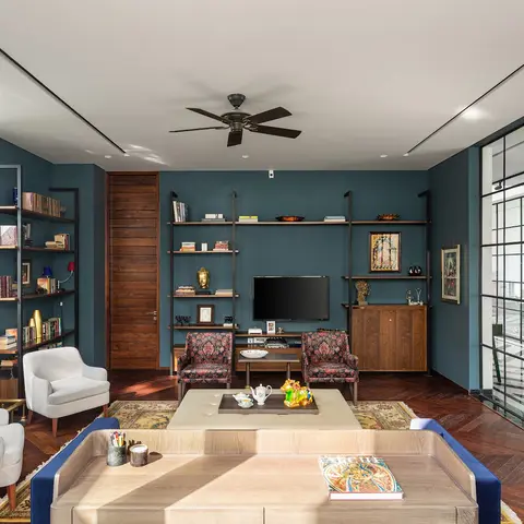 Living room with a deep teal accent wall behind an open metal-and-wood shelving/TV unit, patterned armchairs, a herringbone