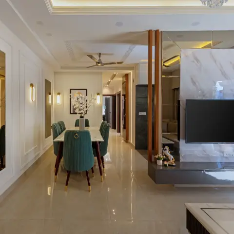An open-plan hallway showing a green channel-tufted velvet dining set on a marble table beside a marble-clad TV feature wall