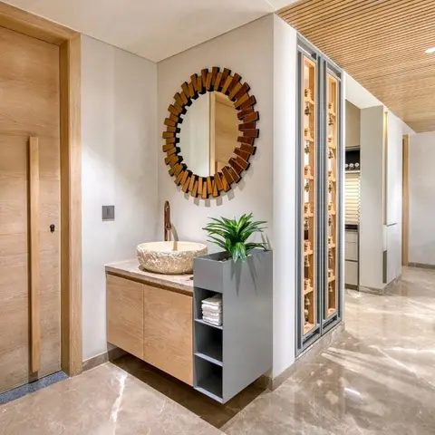 An entrance foyer with a stone vessel wash basin under a sunburst mirror, a wood-slat ceiling, and a marble floor leading to