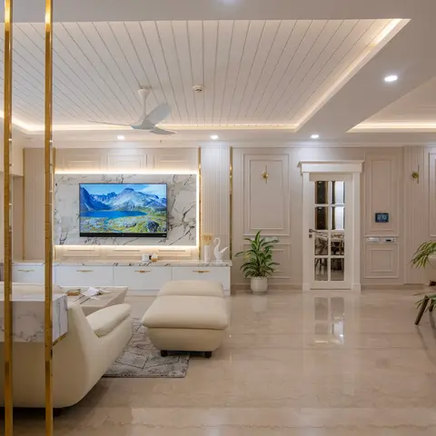 Open living area with a marble-clad TV wall framed by brass rods, fluted wall panelling, a cove-lit stepped ceiling, and