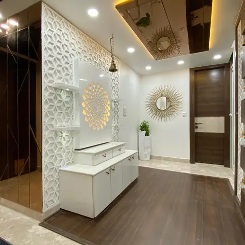 Entrance foyer with a white jaali-panel wall featuring a backlit Om motif niche and hanging brass bell, a glossy white