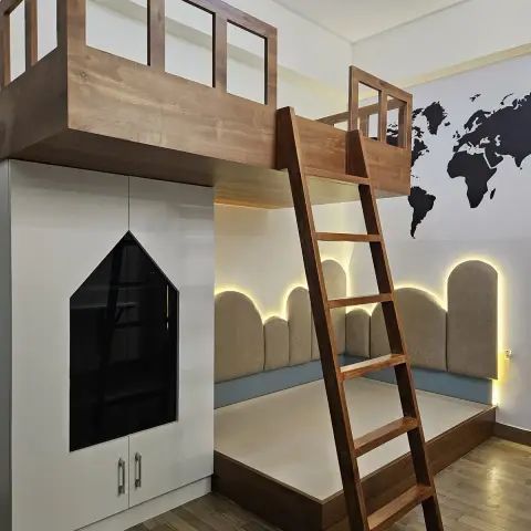 Kids' loft bed with a wooden treehouse-style railing and ladder above a cushioned daybed nook, beside a wardrobe with a