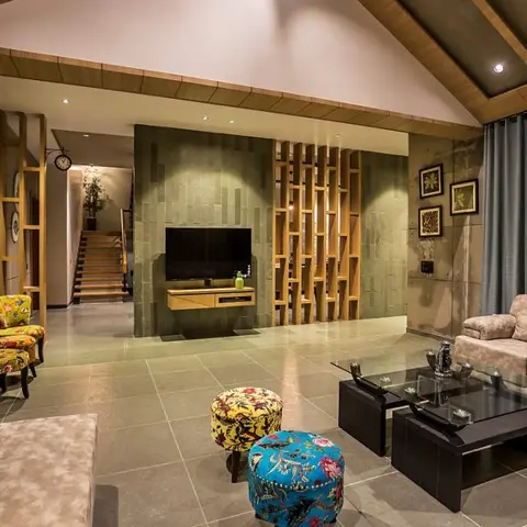 Living room with a stone-clad TV wall flanked by a wood slat screen, sloped wood ceiling, and colorful floral ottomans in