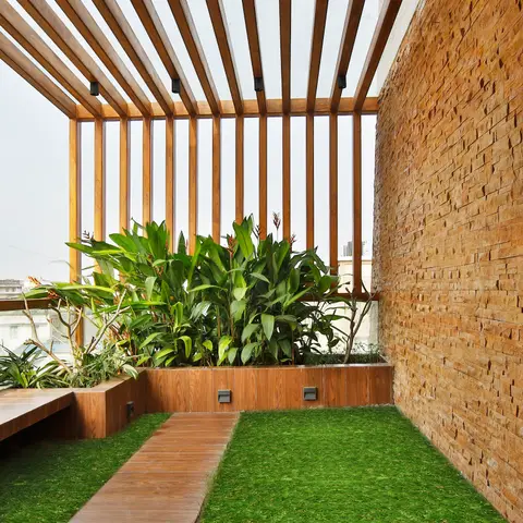 Rooftop terrace with a timber pergola, a stone-clad wall, and a wood boardwalk crossing an artificial-grass lawn framed by